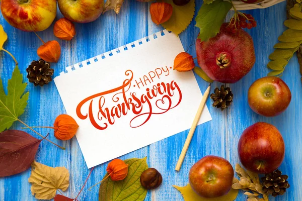 Thanksgiving - letters. Autumn bright background. Flowers, leaves and fruits on a blue wooden background. Background for the autumn holidays and thanksgiving day.