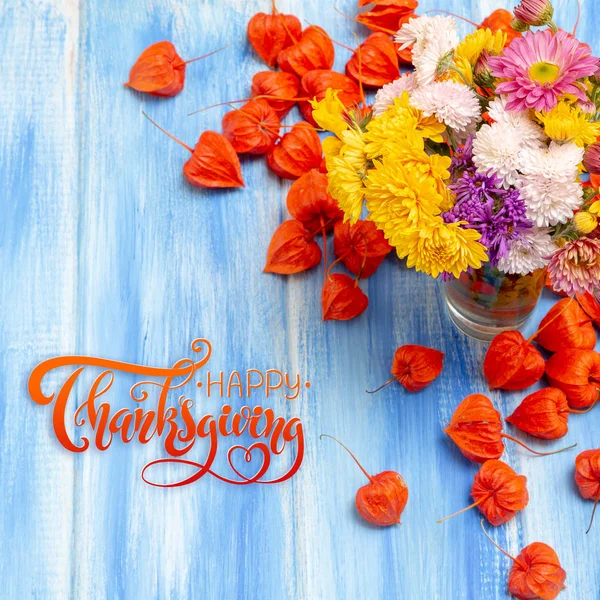 Thanksgiving - letters. Autumn background. Bright orange physalis berries on a blue woody background. Congratulations for the autumn holidays and thanksgiving day.