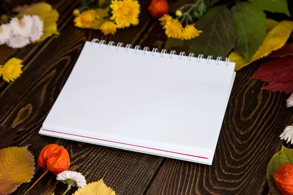 Autumn bright background. Notebook for the inscription. Flowers, leaves and fruits on a brown wooden background. Background for the autumn holidays and thanksgiving day.