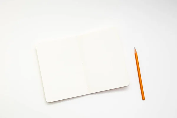 Notebook and pencil on white background. Workplace of the artist or writer. Kraft paper, top view.
