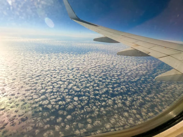 View from the window of the plane. In the window you can see the wing of the aircraft, the earth and the mountains. blue sky and clouds. Natural natural background. The theme of tourism and travel. — Stock Photo, Image