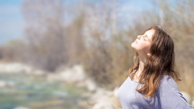 Olumlu duyguları olan genç bir kız. Rahatlamış, yüzünde bir gülümsemeyle mutlu. İlkbahar doğal arka plan, orman ve nehir.