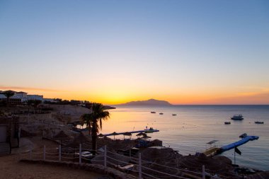 Kızıldeniz'de gün doğumu. Güneş ışınları ve sabah bulutları ile güzel parlak gökyüzü. Deniz ve tekneler. Tiran Adası manzarası. Mısır, Şarm El Şeyh. Turizm ve seyahat.