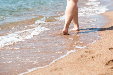 Sahilde çıplak ayakların yakın çekim. Suyun kenarında kumda yürüyorum. Tatil ve seyahat konsepti. Kadın bacakları. Kozmetik ve vücut bakımı. Plaj seyahat - kum plajda kadın bacaklar