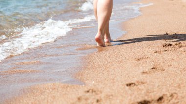 Sahilde çıplak ayakların yakın çekim. Suyun kenarında kumda yürüyorum. Tatil ve seyahat konsepti. Kadın bacakları. Kozmetik ve vücut bakımı. Plaj seyahat - kum plajda kadın bacaklar