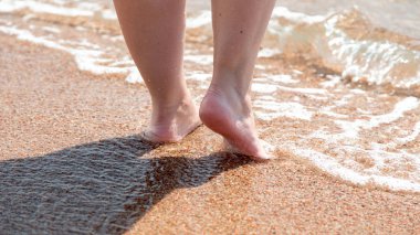 Sahilde çıplak ayakların yakın çekim. Suyun kenarında kumda yürüyorum. Tatil ve seyahat konsepti. Kadın bacakları. Kozmetik ve vücut bakımı. Plaj seyahat - kum plajda kadın bacaklar