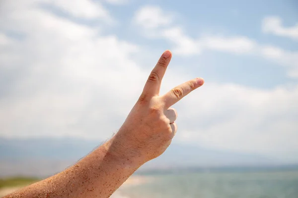 male hand shows 2 fingers or victory sign. Against the sky and the sea. Rest and relaxation