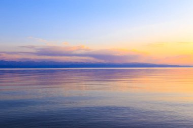 Dağlardaki bir gölde güzel gün batımı. Kırgızistan, İssyk-Kul Gölü. Parlak gökyüzü, sıcak renklerde arka plan.