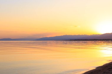 Dağlardaki bir gölde güzel gün batımı. Kırgızistan, İssyk-Kul Gölü. Parlak gökyüzü, sıcak renklerde arka plan.