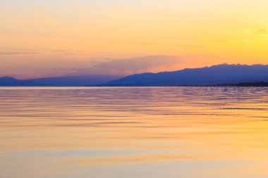 Dağlardaki bir gölde güzel gün batımı. Kırgızistan, İssyk-Kul Gölü. Parlak gökyüzü, sıcak renklerde arka plan.