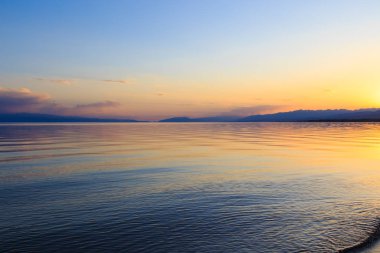 Dağlardaki bir gölde güzel gün batımı. Kırgızistan, İssyk-Kul Gölü. Parlak gökyüzü, sıcak renklerde arka plan.