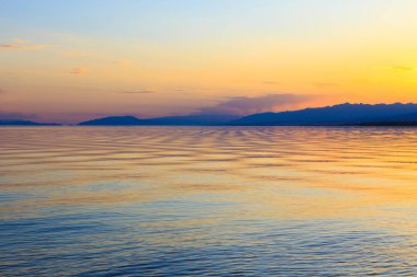 Dağlardaki bir gölde güzel gün batımı. Kırgızistan, İssyk-Kul Gölü. Parlak gökyüzü, sıcak renklerde arka plan.