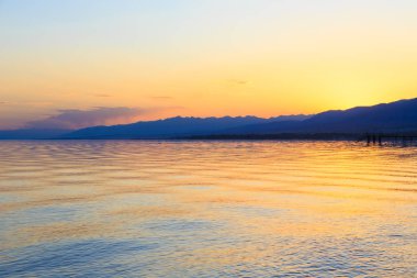 Dağlardaki bir gölde güzel gün batımı. Kırgızistan, İssyk-Kul Gölü. Parlak gökyüzü, sıcak renklerde arka plan.