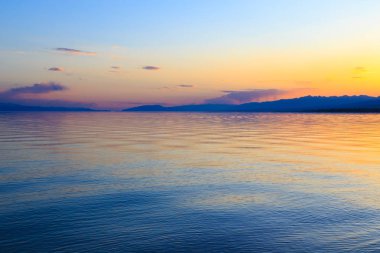 Dağlardaki bir gölde güzel gün batımı. Kırgızistan, İssyk-Kul Gölü. Parlak gökyüzü, sıcak renklerde arka plan.