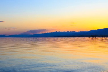 Dağlardaki bir gölde güzel gün batımı. Kırgızistan, İssyk-Kul Gölü. Parlak gökyüzü, sıcak renklerde arka plan.