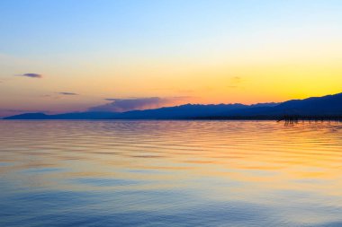 Dağlardaki bir gölde güzel gün batımı. Kırgızistan, İssyk-Kul Gölü. Parlak gökyüzü, sıcak renklerde arka plan.