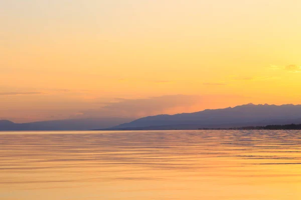 Hermosa puesta de sol en un lago en las montañas. Kirguistán, lago Issyk-Kul. Cielo brillante, fondo en colores cálidos . —  Fotos de Stock