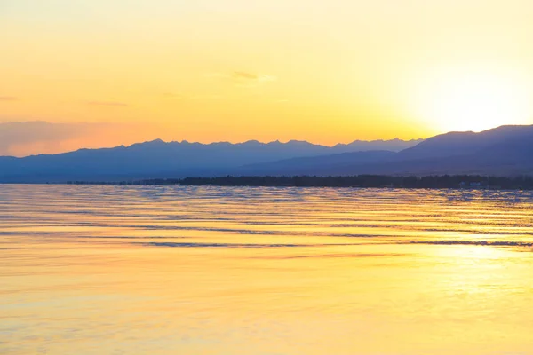 Hermosa puesta de sol en un lago en las montañas. Kirguistán, lago Issyk-Kul. Cielo brillante, fondo en colores cálidos . — Foto de Stock