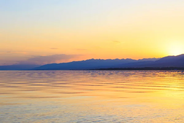 Matahari terbenam yang indah di danau di pegunungan. Kirgizstan, Danau Issyk-Kul. Langit cerah, latar belakang dalam warna hangat . — Stok Foto