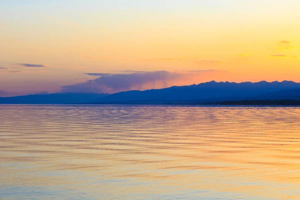 Matahari terbenam yang indah di danau di pegunungan. Kirgizstan, Danau Issyk-Kul. Langit cerah, latar belakang dalam warna hangat . — Stok Foto