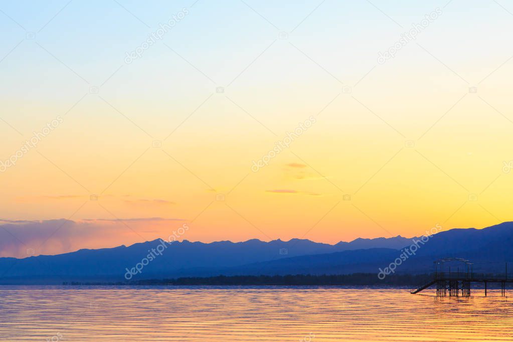 Beautiful sunset on a lake in the mountains. Kyrgyzstan, Issyk-Kul Lake. Bright sky, background in warm colors.