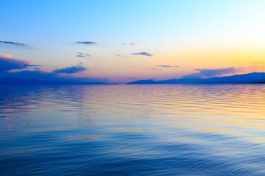 Dağlardaki bir gölde güzel gün batımı. Kırgızistan, İssyk-Kul Gölü. Parlak gökyüzü, sıcak renklerde arka plan.