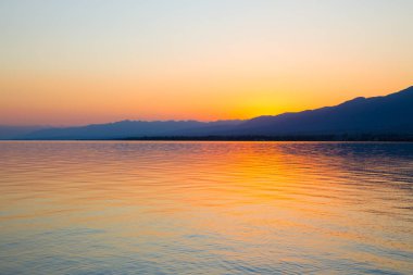 Dağlardaki bir gölde güzel gün batımı. Kırgızistan, İssyk-Kul Gölü. Parlak gökyüzü, sıcak renklerde arka plan.