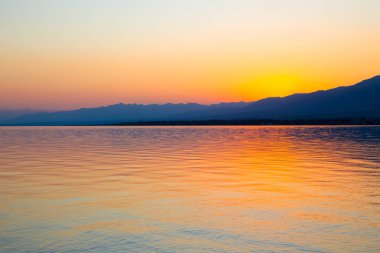 Dağlardaki bir gölde güzel gün batımı. Kırgızistan, İssyk-Kul Gölü. Parlak gökyüzü, sıcak renklerde arka plan.