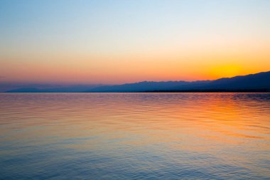 Dağlardaki bir gölde güzel gün batımı. Kırgızistan, İssyk-Kul Gölü. Parlak gökyüzü, sıcak renklerde arka plan.