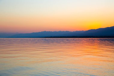 Dağlardaki bir gölde güzel gün batımı. Kırgızistan, İssyk-Kul Gölü. Parlak gökyüzü, sıcak renklerde arka plan.
