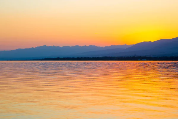 Belo pôr-do-sol num lago nas montanhas. Quirguizistão, Lago Issyk-Kul. Céu brilhante, fundo em cores quentes . — Fotografia de Stock