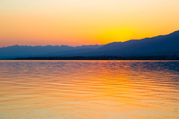 Hermosa puesta de sol en un lago en las montañas. Kirguistán, lago Issyk-Kul. Cielo brillante, fondo en colores cálidos . — Foto de Stock