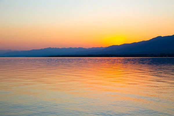 Hermosa puesta de sol en un lago en las montañas. Kirguistán, lago Issyk-Kul. Cielo brillante, fondo en colores cálidos . — Foto de Stock