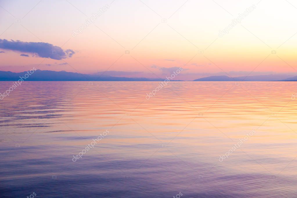 Beautiful sunset on a lake in the mountains. Kyrgyzstan, Issyk-Kul Lake. Bright sky, background in warm colors.