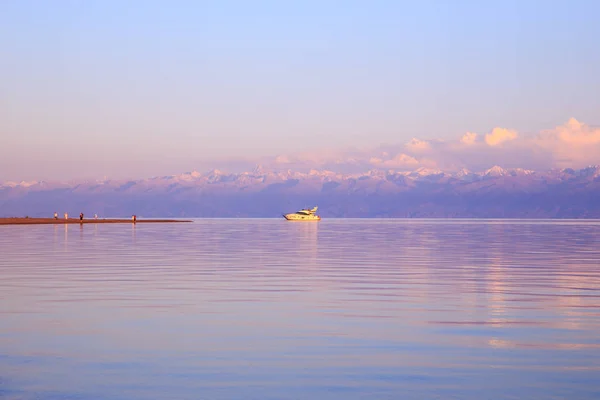 Bílá jachta na vodě v paprscích zapadajícího slunce. Kyrgyzstán, jezero Issyk-kule. Světlá obloha, pozadí v teplých barvách. — Stock fotografie
