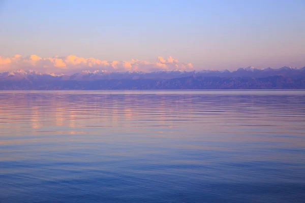 Nádherný západ slunce na jezeře v horách. Kyrgyzstán, jezero Issyk-kule. Světlá obloha, pozadí v teplých barvách. — Stock fotografie