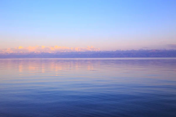 Hermosa puesta de sol en un lago en las montañas. Kirguistán, lago Issyk-Kul. Cielo brillante, fondo en colores cálidos . — Foto de Stock