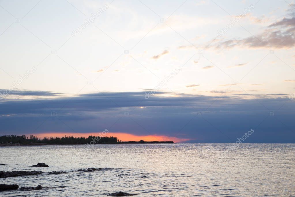 Beautiful sunset on a lake in the mountains. Kyrgyzstan, Issyk-Kul Lake. Bright sky, background in warm colors.