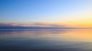 Dağlardaki bir gölde güzel gün batımı. Kırgızistan, İssyk-Kul Gölü. Parlak gökyüzü, sıcak renklerde arka plan.