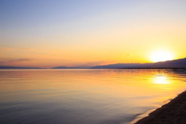Dağlardaki bir gölde güzel gün batımı. Kırgızistan, İssyk-Kul Gölü. Parlak gökyüzü, sıcak renklerde arka plan.