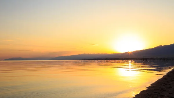 Hermosa puesta de sol en un lago en las montañas. Kirguistán, lago Issyk-Kul. Cielo brillante, fondo en colores cálidos . — Foto de Stock