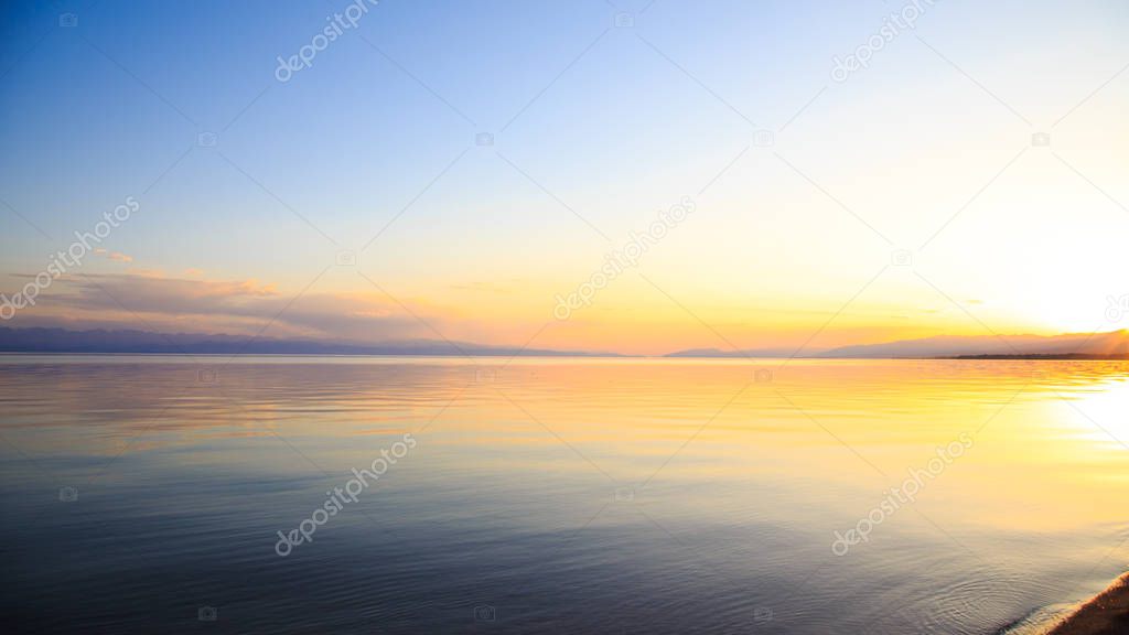 Beautiful sunset on a lake in the mountains. Kyrgyzstan, Issyk-Kul Lake. Bright sky, background in warm colors.