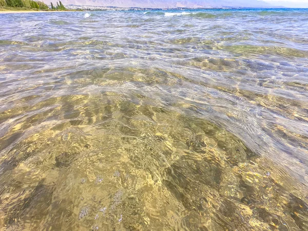 La texture dell'acqua limpida con fondo sabbioso. Onda sulla riva del mare o sull'oceano . — Foto Stock