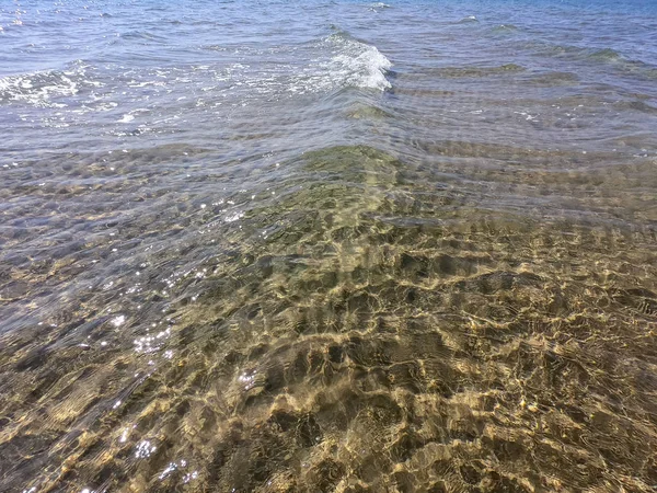 La textura del agua clara con fondo arenoso. Ola en la orilla del mar o el océano . — Foto de Stock