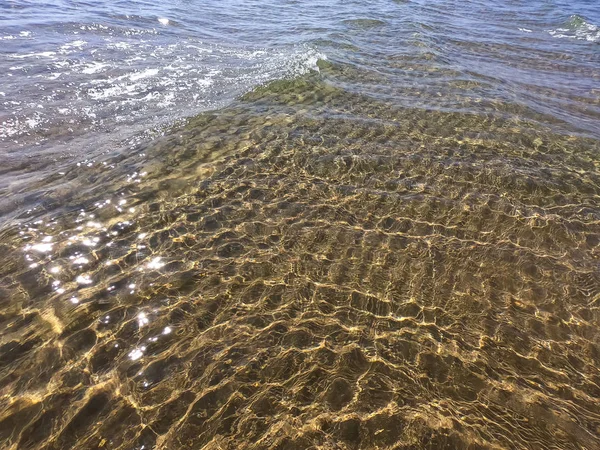 De textuur van helder water met zanderige bodem. Golf aan de kust of Oceaan. — Stockfoto