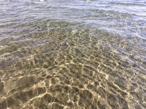 La textura del agua clara con fondo arenoso. Ola en la orilla del mar o el océano . — Foto de Stock