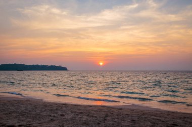 denizde gün batımı. kumlu plaj, berrak su, dalgalar. batan güneşin sıcak renklerde sörf hattı.