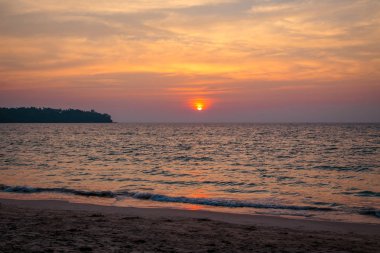 denizde gün batımı. kumlu plaj, berrak su, dalgalar. batan güneşin sıcak renklerde sörf hattı.