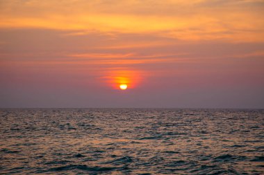 denizde gün batımı. kumlu plaj, berrak su, dalgalar. batan güneşin sıcak renklerde sörf hattı.