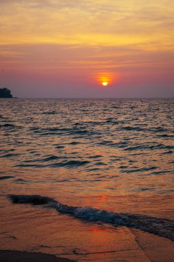 denizde gün batımı. kumlu plaj, berrak su, dalgalar. batan güneşin sıcak renklerde sörf hattı.